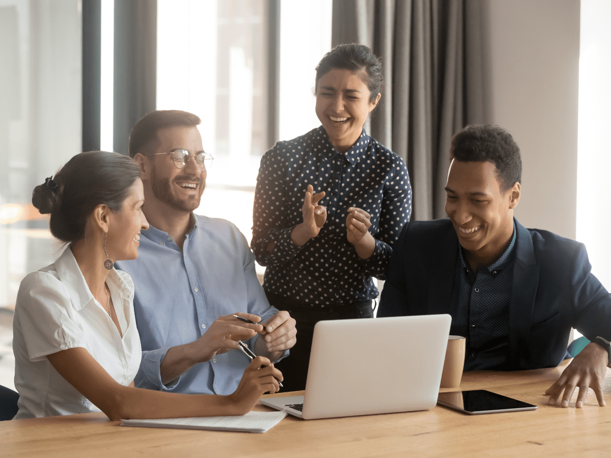 Team celebrating success around laptop in office meeting.
