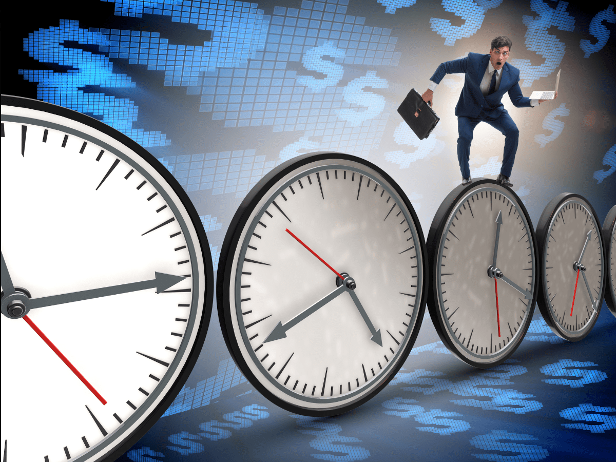 Businessman balancing on clocks amid financial pressure.