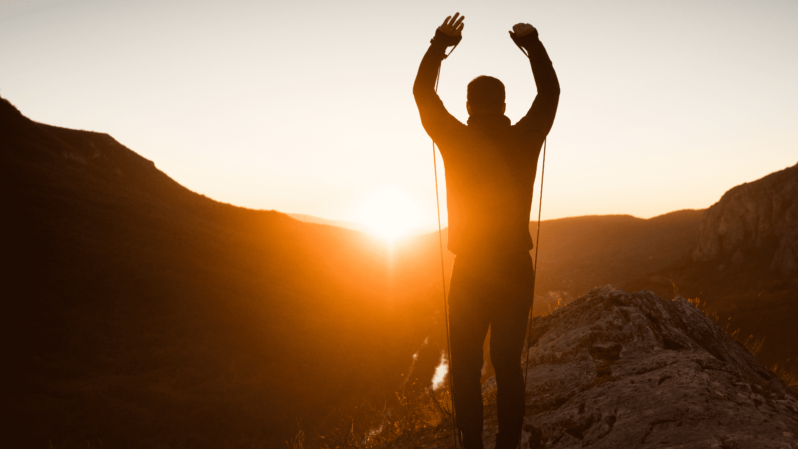 Silhouette of hiker celebrating sunrise atop rugged mountain ridge.